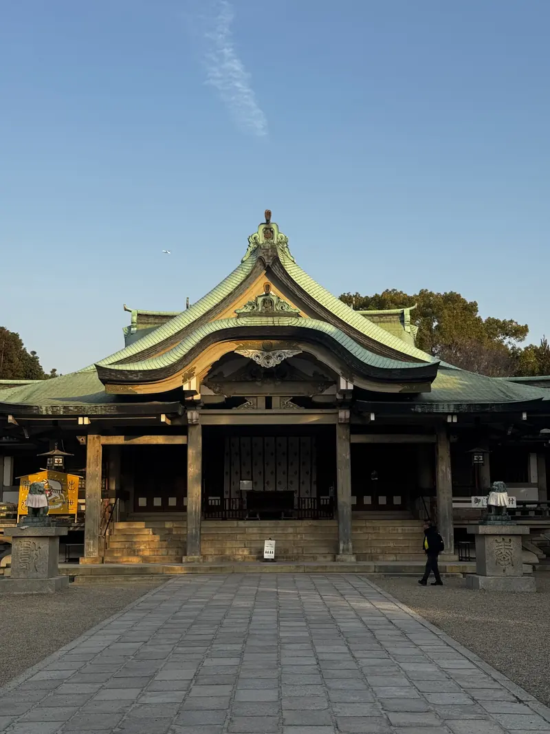 Un santuario japonés de techo verde al fondo de una plaza empedrada vacía